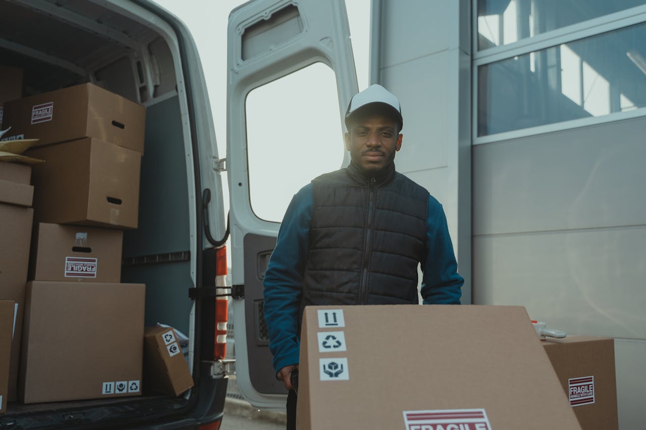 Man in Blue and Black Jacket Standing Beside Brown Cardboard Box